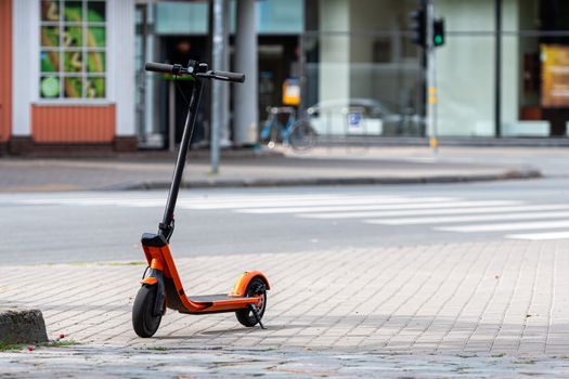 electric scooter or e-scooter parked on sidewalk, blurred city street background - image