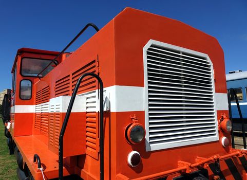 A vintage diesel engine in red and white against a blue sky
