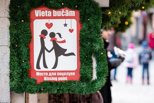 Sign with human silhouettes and inscription KISSING POINT in Latvian, Russian and English at log cabin at Christmas market, Riga, Latvia - image