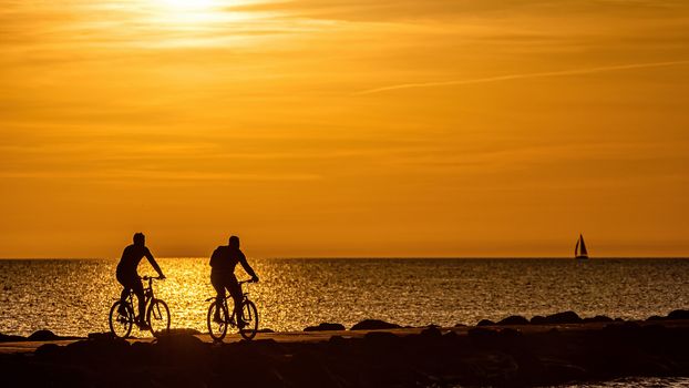 silhouette of people walking and biking on the pier during the golden hour of sunset
