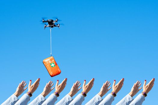 many human hands receiving the first aid kit with coronavirus medication from flying drone, concept for delivery of COVID-19 virus medication using modern technology