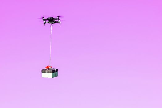 multicopter drone flying with a gift box isolated on a pink background, concept of modern fast delivery method by using drones