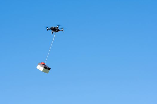 multicopter drone flying with a gift box isolated on a blue sky, concept of modern fast delivery method by using drones