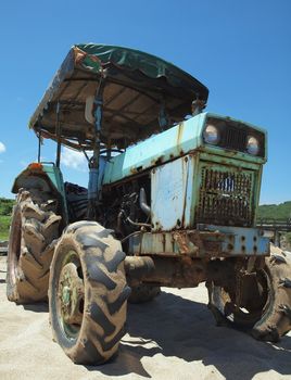 A vintage tractor sits on a sand beach against a blue sky
