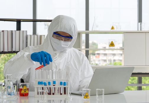 Epidemiological researchers in virus protective clothing mixing chemicals according to formulas obtained from computers. Working atmosphere in chemical laboratory.