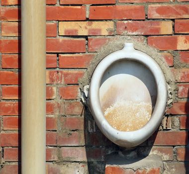 An old ceramic urinal bowl is mounted on a brick wall
