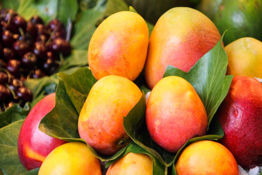 Lot of red fresh mango fruits with leaves at market, food background