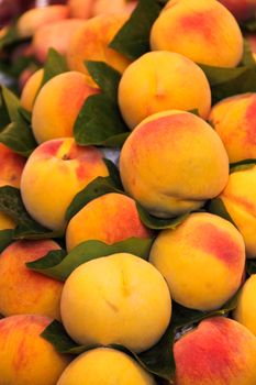 Lot of red fresh peach fruits with leaves at market, food background
