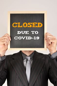 business man with a blackboard and message closed due to covid-19