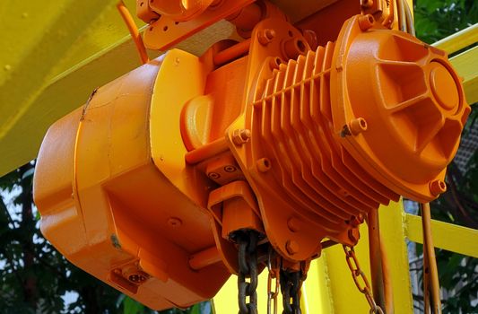 An orange winch with an attached iron chain used for lifting construction materials
