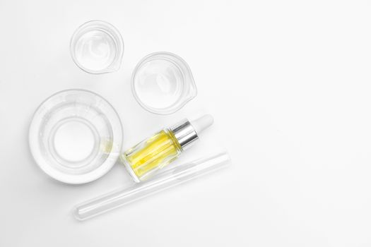 Yellow cosmetic liquid (oil). Chemicals for beauty care on white laboratory table. (Top View)