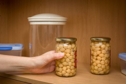 woman picking up a pot of chickpeas from the kitchen pantry