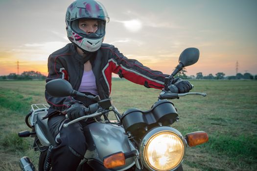 young attractive woman on motorcycle on dirt road at sunset