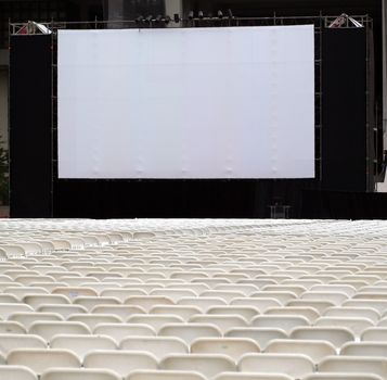 Rows of white plastic chairs are set up for an outdoor movie show

