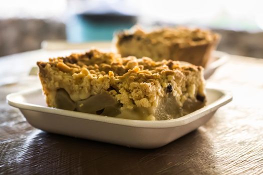 Piece of apple crumble cake on a plastic tray in close-up another one in the background