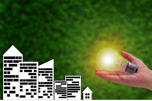 Energy concept, paper city and hand holding light bulb on green background, nature and ecology