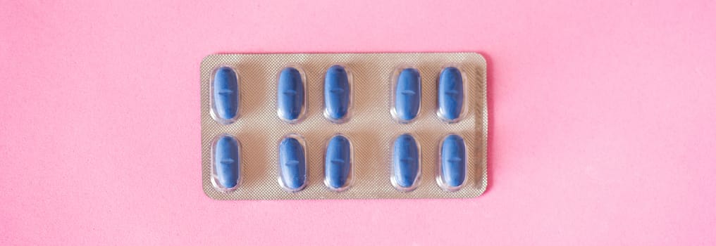 Blue medical pills on pink background. Panorama photo.