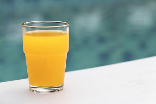 Glass of orange juice placed on a chair by the pool.