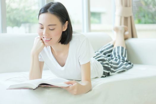 Portrait of a relaxed casual woman reading a book on sofa in a bright house