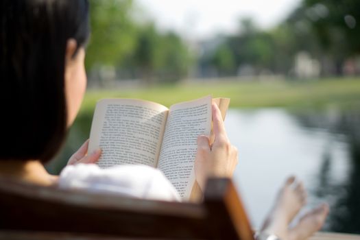 Beautiful young woman reading book on sun lounger by swimming pool