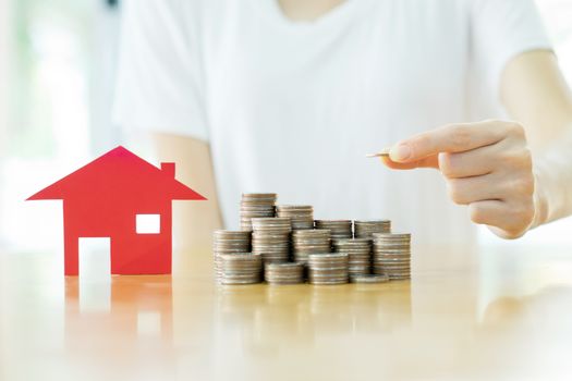 woman put coins to stack of coins and red house blackground