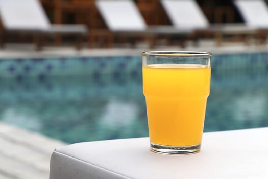 Glass of orange juice placed on a chair by the pool.