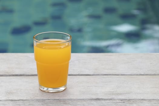 Glass of orange juice placed on a chair by the pool.