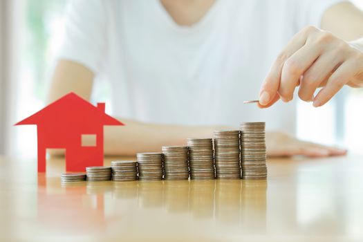 woman put coins to stack of coins and red house blackground