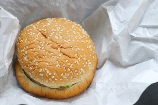 The hamburger is placed on white paper. Hamburger with white sesame sprinkled on top.