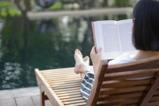 woman reading and relaxing near luxury swimming pool