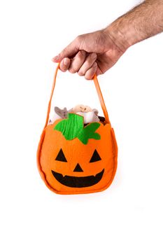 Hand holding Halloween pumpkin bag with candies inside isolated on white background