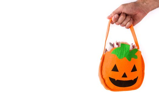 Hand holding Halloween pumpkin bag with candies inside isolated on white background
