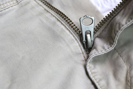 The zipper of the pants that opened. Metal zipper of cream pants.