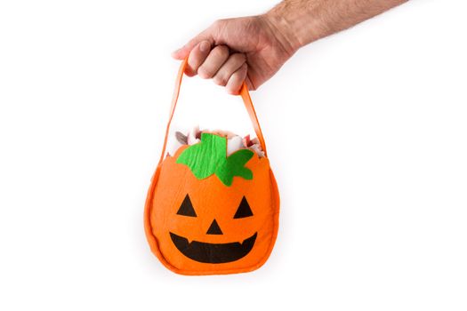 Hand holding Halloween pumpkin bag with candies inside isolated on white background