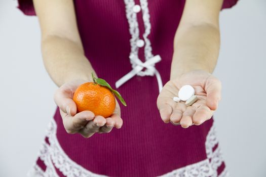 Vitamins from fruits or medicines? A young woman in burgundy pajamas shows a mandarin in her right hand and an aspirin in her left