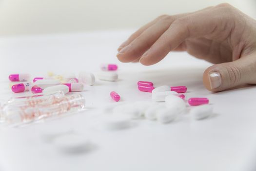 Addiction to medicines and drugs in modern times: close-up shot of a young woman's hand about to grab various tablets and vials on table and white background