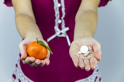 Vitamins from fruits or medicines? A young woman in burgundy pajamas shows a mandarin in her right hand and an aspirin in her left