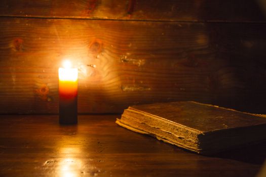 Reading scene in ancient times: an old book leaning on ruined wooden table lighted by a candle on a wooden background