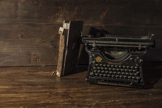 Florence, Italy - 12/20/2018 - Reading and writing scenes in ancient times: an old book he leans tired at an old Underwood typewriter on a ruined wooden table 