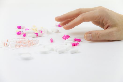 Addiction to medicines and drugs in modern times: close-up shot of a young woman's hand about to grab various tablets and vials on table and white background