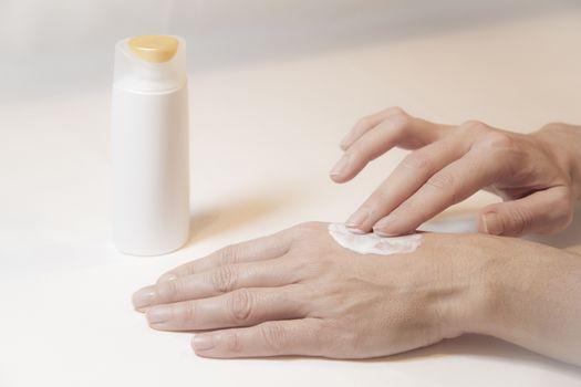 Close up of the hands of a woman who takes care of herself by rubbing cream with two fingers on the back of her left hand