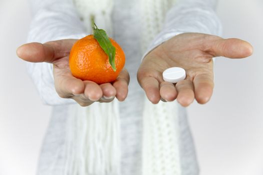 Vitamins from fruit or drugs? A sick young woman with a scarf on her neck shows a mandarin in her right hand and an aspirin on her left