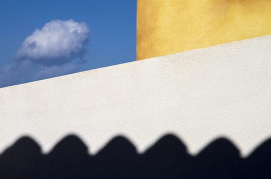 Two exterior walls of the house, white and yellow, bound a small piece of blue sky where a small cloud flies. Below the menacing and black shadow of the cornice weighs the composition balancing it