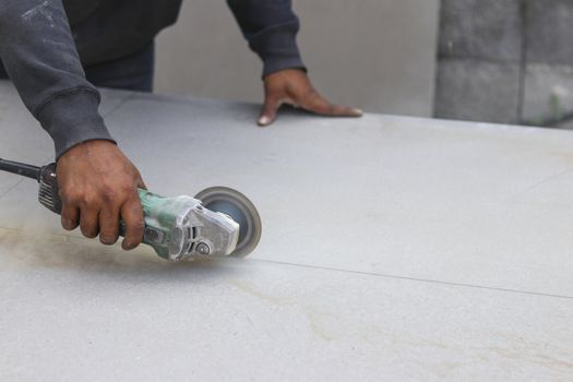 The mechanic is using a grinding machine for cut in half of cement board.