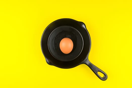 Top view of raw chicken eggs in frying pan on yellow background.
