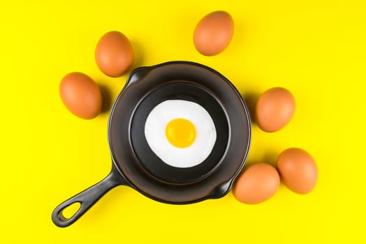 Frying pan with fried egg isolated on a yellow background viewed from above.