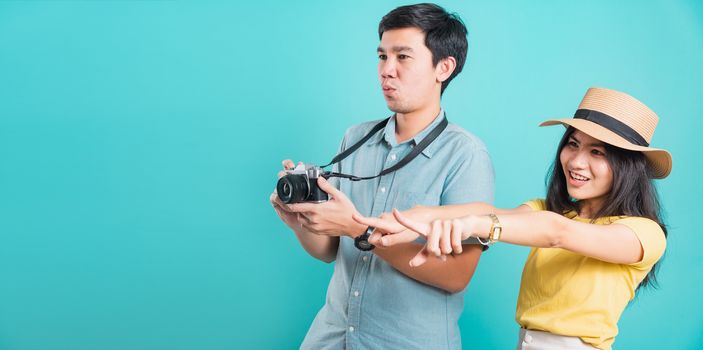 Happy Asian excited couple young beautiful woman point finger and handsome man holding camera shot photography in summer holiday travel tourists isolated on blue background with copy space for text