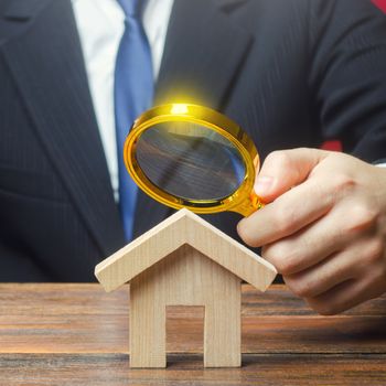 A man is studying a house through a magnifying glass. Fair value of real estate. Property valuation. Legal deal. Standards and quality of construction. Legality and transparency of purchase agreement.