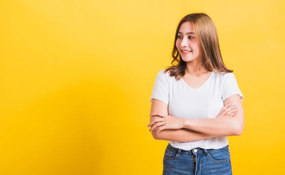 Asian Thai happy portrait beautiful cute young woman standing wear t-shirt her smile confidence with crossed arms looking to side up isolated, studio shot on yellow background and copy space