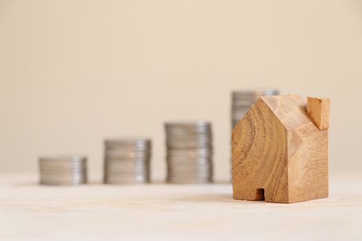 Wooden home model with blurred coins bar graph background.